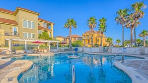 A swimming pool with a fountain, surrounded by palm trees and buildings. - Beautiful gulf-front beach home with sweeping views from balcony, shared pool, WiFi (Gulf Shores)