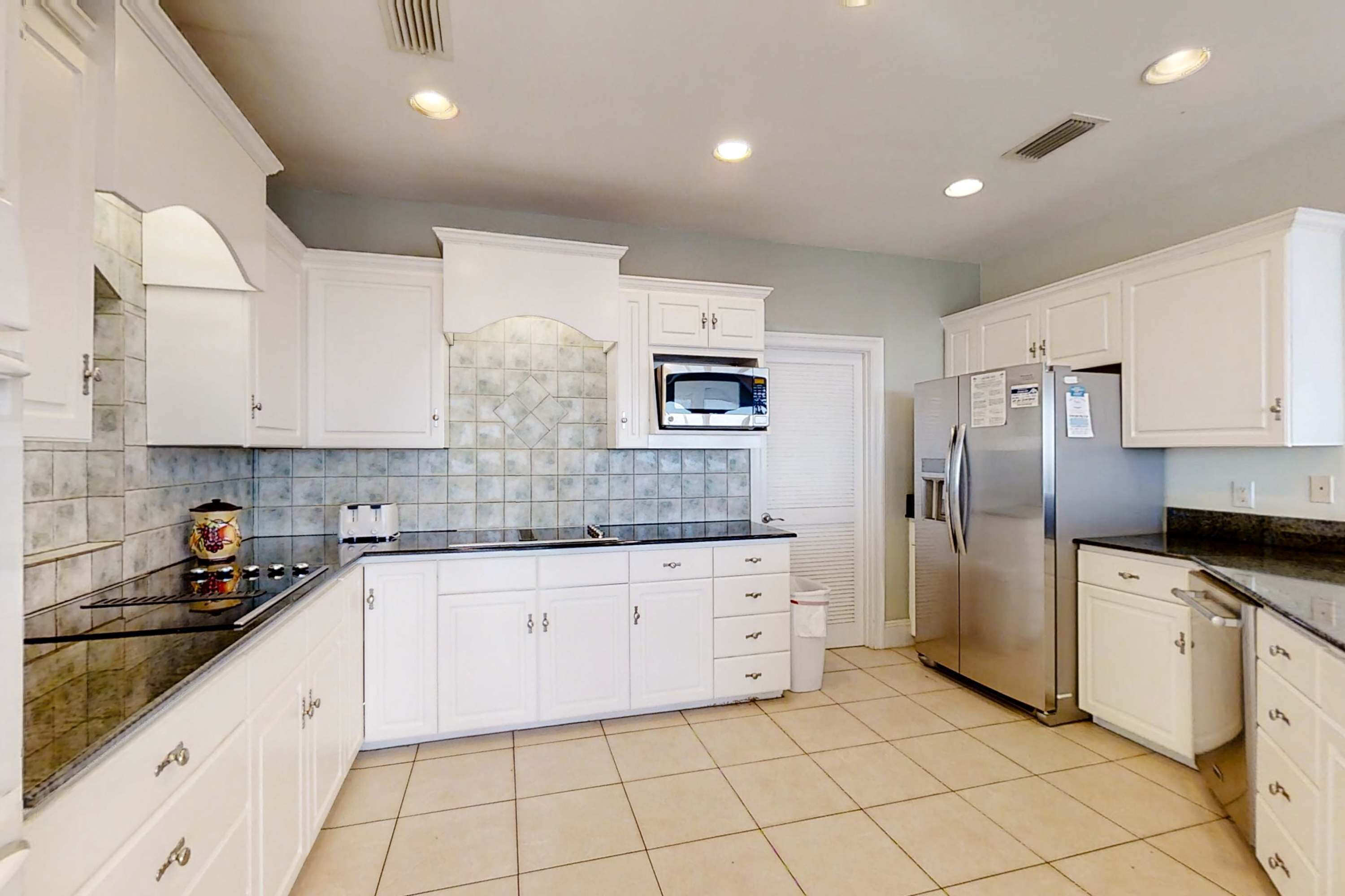 A kitchen with white cabinets, a microwave, a refrigerator, and a tiled backsplash.