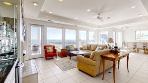 A spacious living room with a high ceiling, large windows, and a view of the city. - Beautiful gulf-front beach home with sweeping views from balcony, shared pool, WiFi (Gulf Shores)
