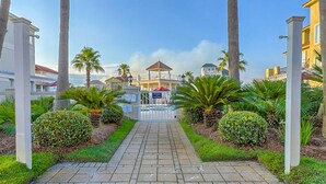 A pathway leading to a gated area with palm trees and a gazebo. - Beautiful gulf-front beach home with sweeping views from balcony, shared pool, WiFi (Gulf Shores)