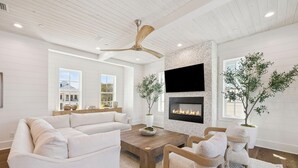 Una sala de estar moderna con chimenea, muebles blancos y un ventilador de techo.