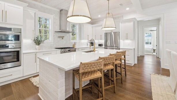 Una cocina moderna con armarios blancos, electrodomésticos de acero inoxidable y una isla grande con taburetes de bar.