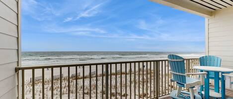 A balcony with a view of the beach, featuring a railing, a table, and two chairs.