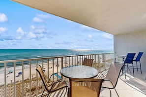 A balcony with a view of the beach and ocean, furnished with chairs and a table. - Elegant, Gulf-front condo with amazing view, pool, covered balcony, W/D & AC (Gulf Shores)