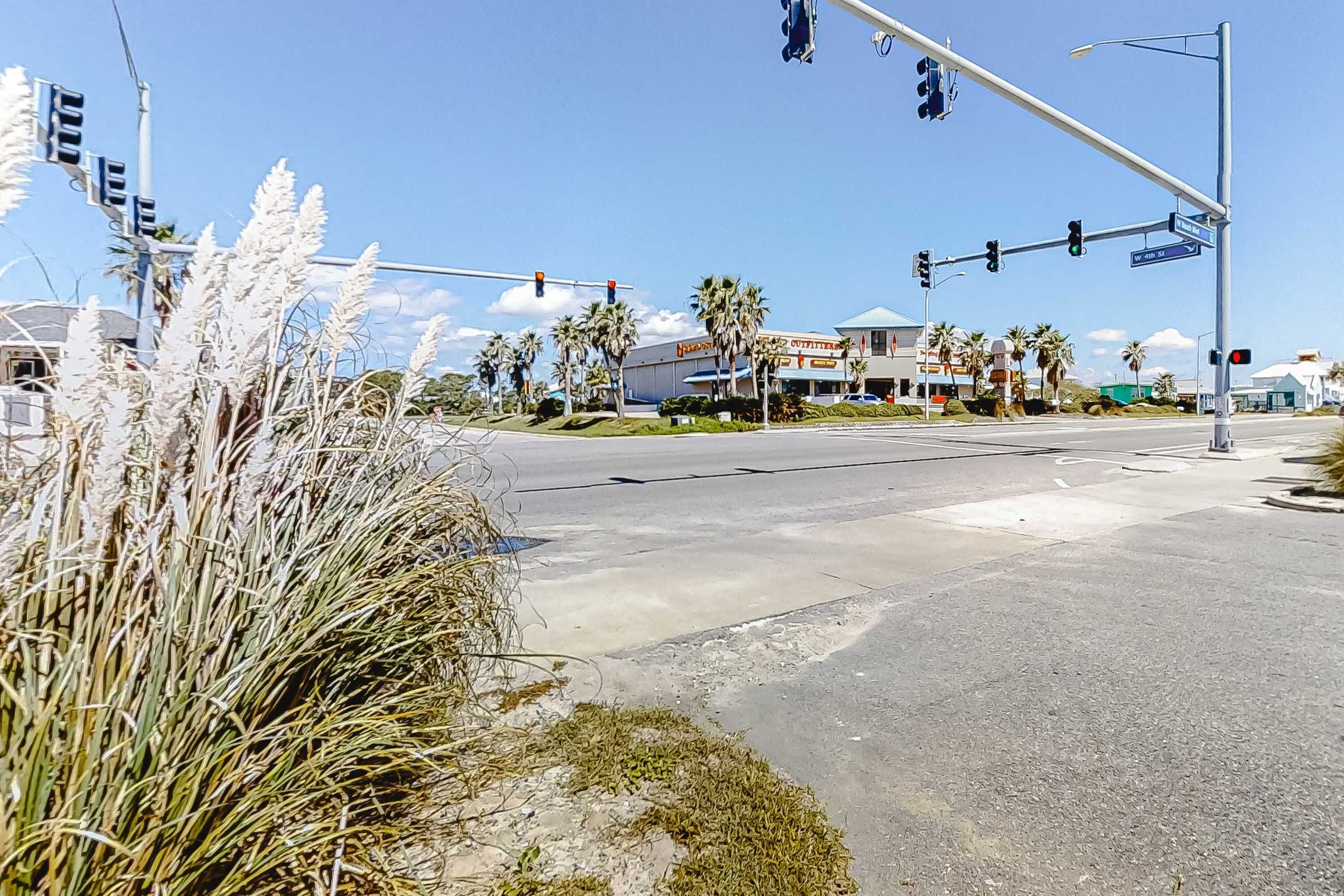 A street intersection with traffic lights, palm trees, and a building with a sign.