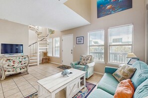 A living room with a TV, a staircase, a sofa, and a painting. - Lofty Condo in a Beachfront Complex w/ WiFi, AC, Balcony & Shared Outdoor Pool (Gulf Shores)