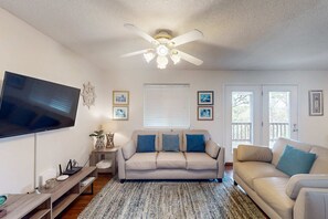 A living room with a ceiling fan, a flat-screen TV, a beige sofa, and a coffee table. - Entire Gulf view duplex with decks, beach access & shared pool, hot tub (Gulf Shores/Fort Morgan)