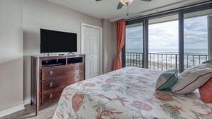 A bedroom with a bed, a dresser, a television, a ceiling fan, and a balcony with a view. - Gulf front condo with beach views, pools & free WiFi (Orange Beach)