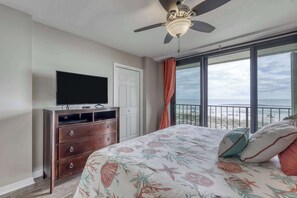 A bedroom with a bed, a dresser, a television, a ceiling fan, and a balcony with a view. - Gulf front condo with beach views, pools & free WiFi (Orange Beach)