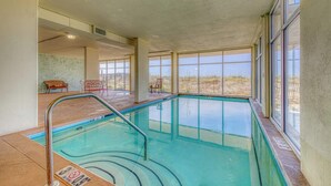 An indoor swimming pool with clear glass walls, a metal pool ladder, and a view of the outdoors. - Gulf front condo with beach views, pools & free WiFi (Orange Beach)
