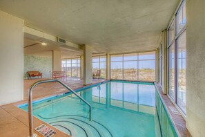 An indoor swimming pool with clear glass walls, a metal pool ladder, and a view of the outdoors. - Gulf front condo with beach views, pools & free WiFi (Orange Beach)