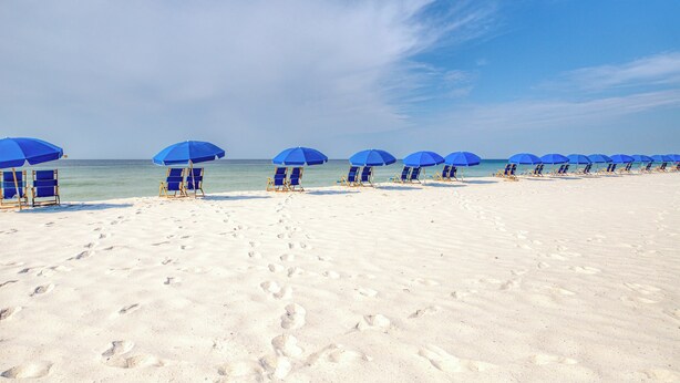 A beach with rows of blue umbrellas and beach chairs. - Gulf front condo with beach views, pools & free WiFi (Orange Beach)