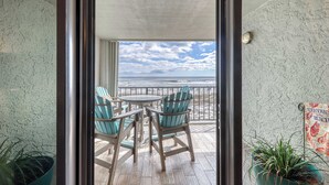 A balcony with a wooden floor, two chairs, and a table. - Gulf front condo with beach views, pools & free WiFi (Orange Beach)