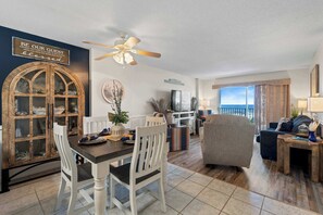 A dining area with a wooden table and chairs, a ceiling fan, and a view of the ocean. - Waterview condo with shared pool, panoramic balcony views, and WIFI (Gulf Shores)