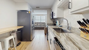 Une cuisine moderne avec des meubles blancs, un plan de travail en marbre et un four encastré.