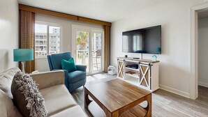 Una sala de estar con un sofá, una mesa de centro, un televisor y una ventana con vistas a edificios.