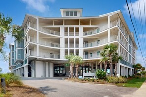 Ein mehrstöckiges Hotel mit Balkonen, einer überdachten Eingangshalle und Palmen.