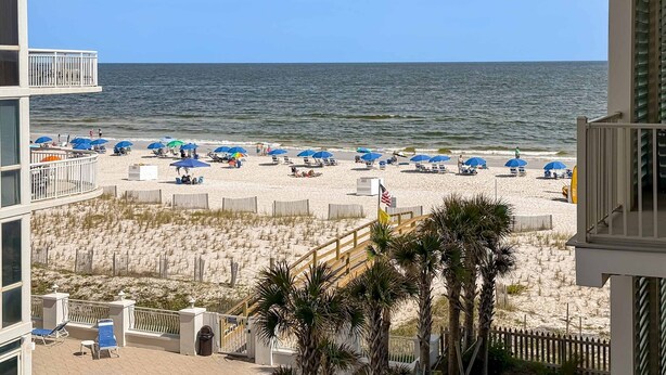 Uitzicht op een strand vanaf een balkon met meerdere niveaus, een zandstrand met parasols en een heldere lucht.