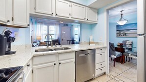 Una cocina con armarios blancos, lavavajillas y comedor con mesa y sillas.