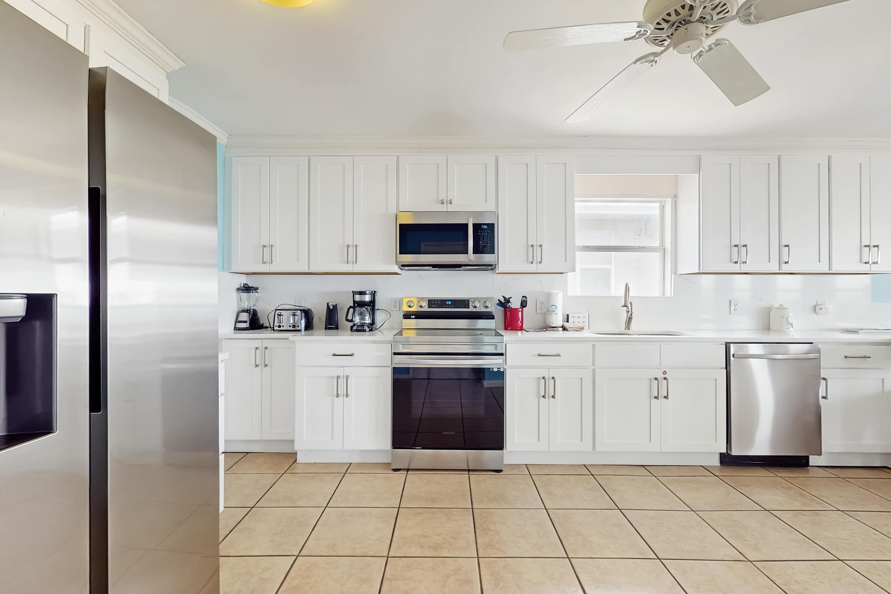 A modern kitchen with white cabinets, stainless steel appliances, and a ceiling fan.