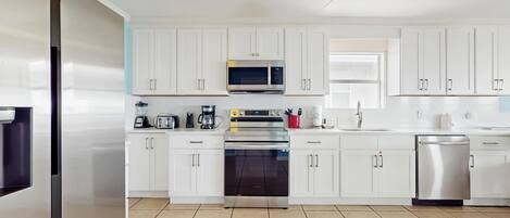 A modern kitchen with white cabinets, stainless steel appliances, and a ceiling fan.
