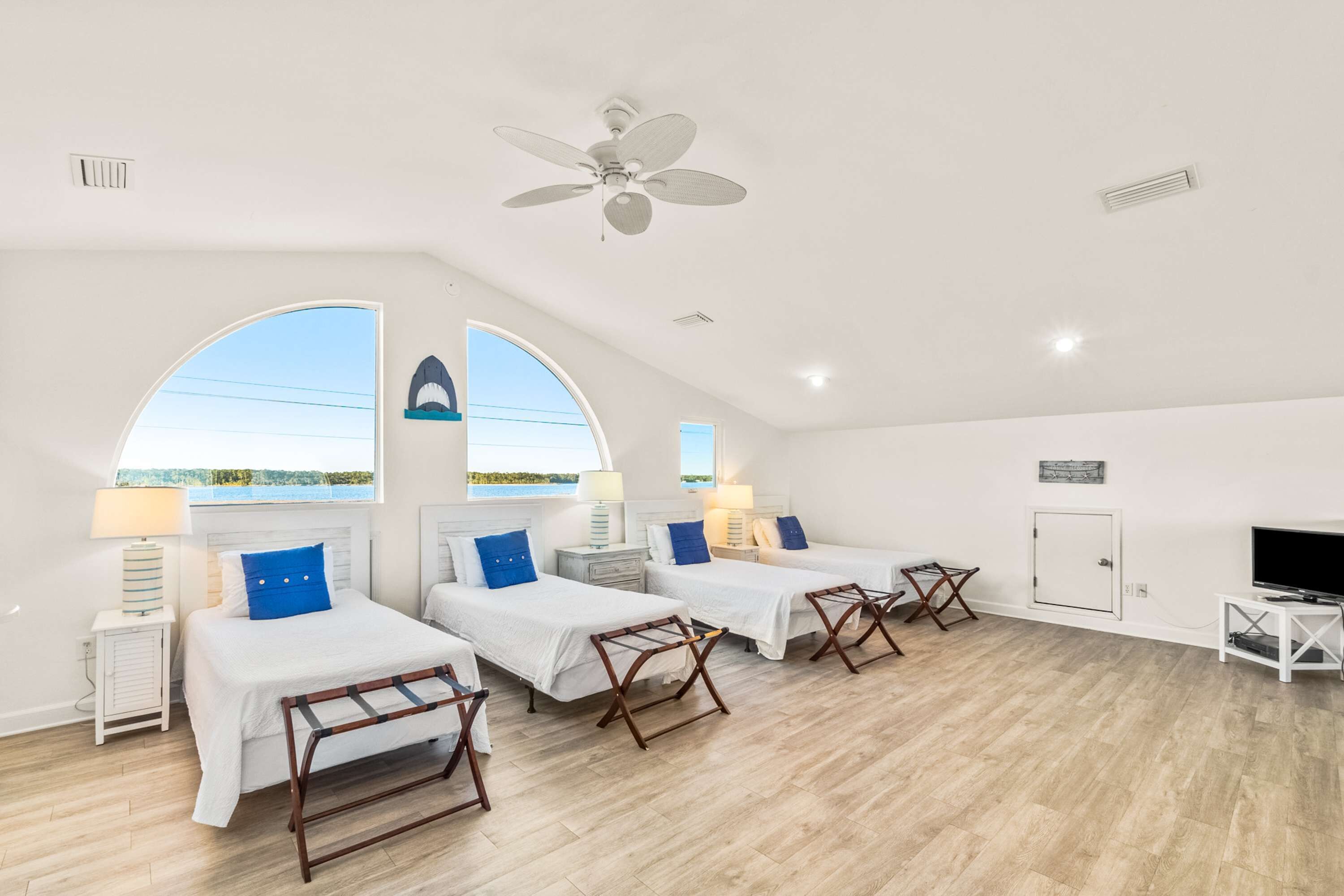 A room with three beds, a ceiling fan, a TV, and a view of the sea.
