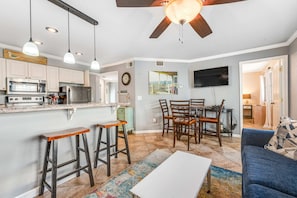 A modern kitchen with a dining area, bar stools, and a ceiling fan. - Convenient and Comfortable Suite in Beachfront Resort w/Shared Pool, Free WiFi (Orange Beach)