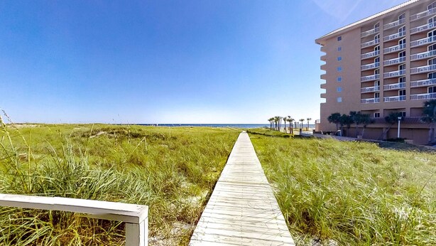 Een pad dat naar een hotel aan het strand leidt, onder een heldere lucht.