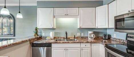 A kitchen with white cabinets, a stainless steel dishwasher, a double oven, and a granite countertop.