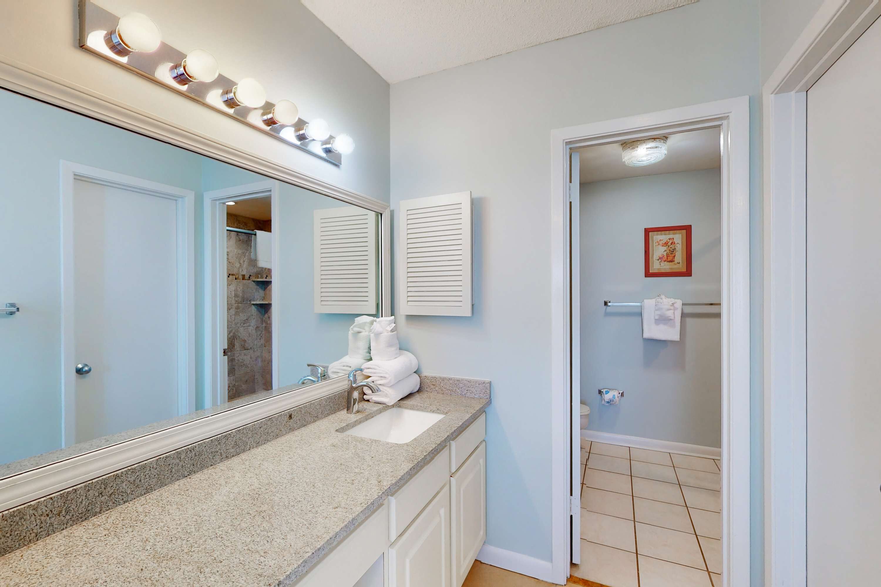 A bathroom with a large mirror, vanity, and lights.