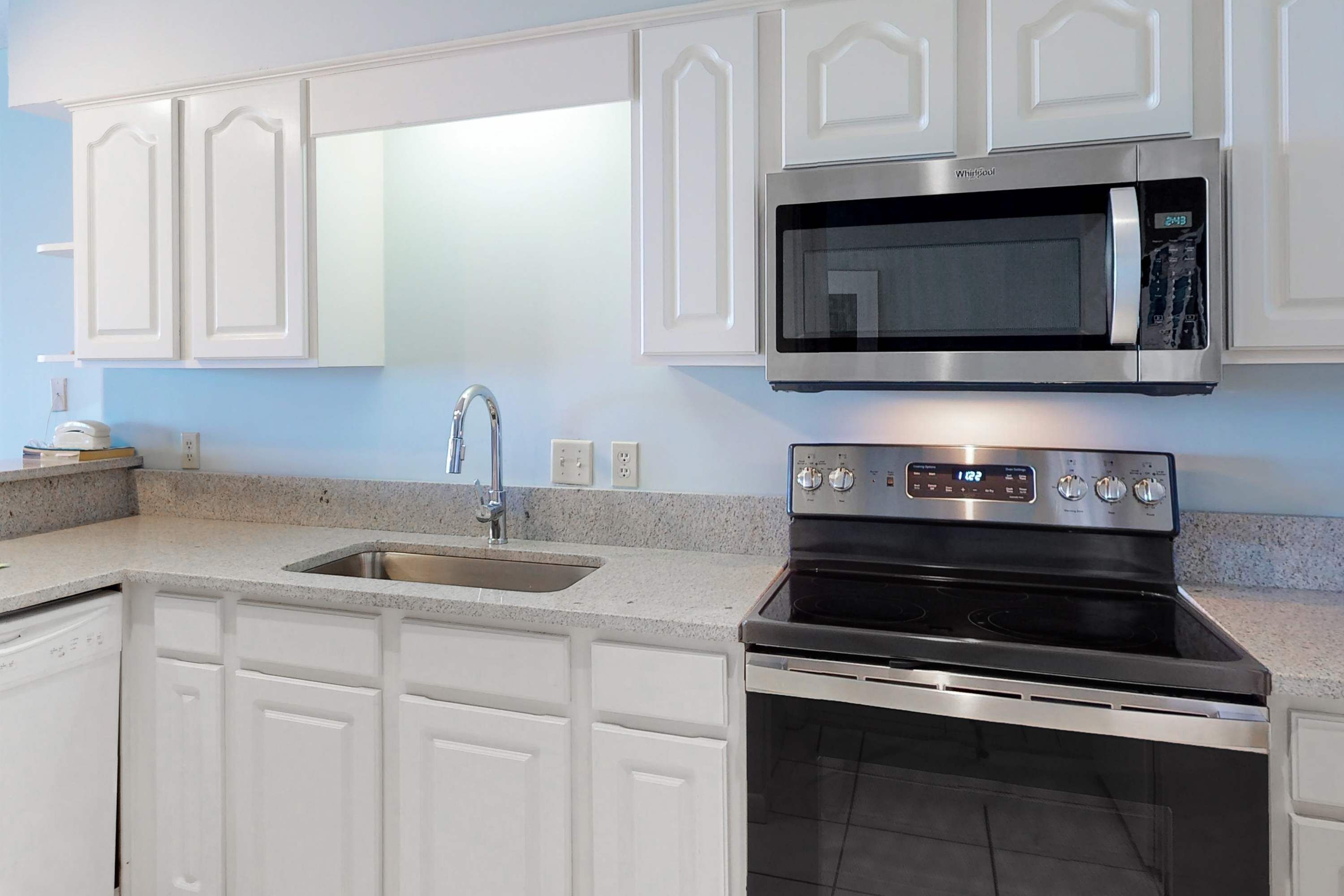 A kitchen with white cabinetry, a stainless steel microwave, and a stove.