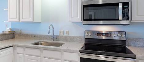 A kitchen with white cabinetry, a stainless steel microwave, and a stove.