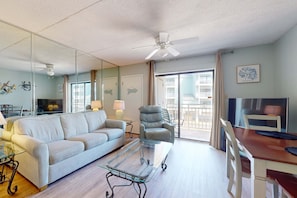Ein Wohnzimmer mit einer Couch, einem Glastisch, einem Sessel, einem Fernseher und einem Balkon mit Blick.