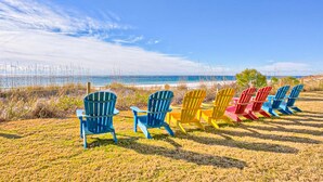 A row of colorful Adirondack chairs facing a beach with a clear sky. - Excellent resort suite in beachfront location with WiFi, pool & elevator (Orange Beach)