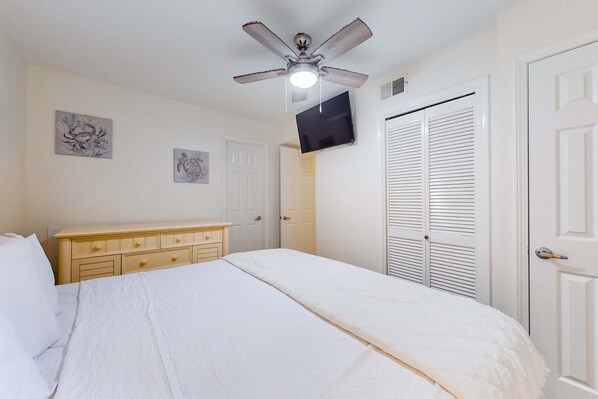 A bedroom with a bed, a ceiling fan, a dresser, a TV, and a closet. - Excellent resort suite in beachfront location with WiFi, pool & elevator (Orange Beach)