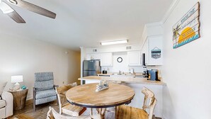 A modern kitchen with white cabinets, a built-in island, and a dining area with a round wooden table and chairs. - Excellent resort suite in beachfront location with WiFi, pool & elevator (Orange Beach)