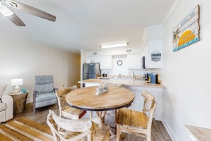 A modern kitchen with white cabinets, a built-in island, and a dining area with a round wooden table and chairs. - Excellent resort suite in beachfront location with WiFi, pool & elevator (Orange Beach)