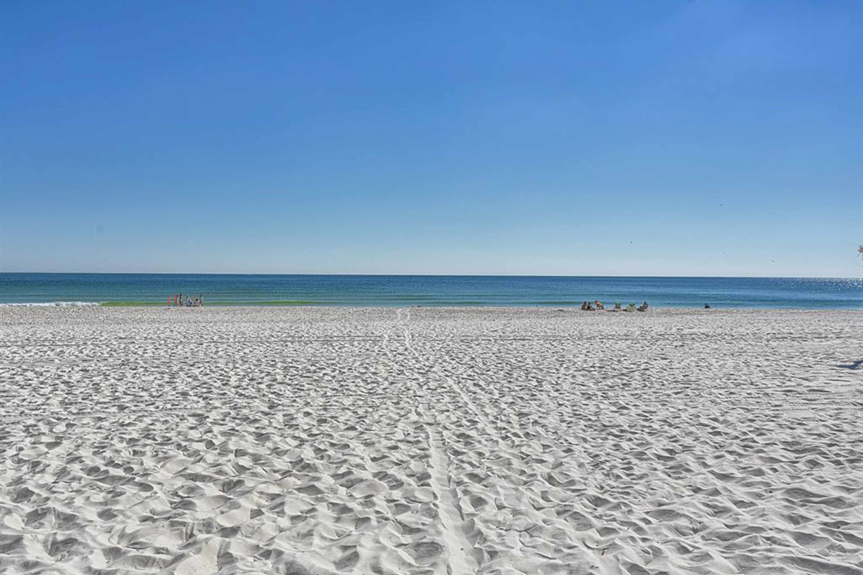 Uma extensa praia de areia dourada, com céu azul límpido e mar tranquilo.