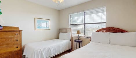 A bedroom with two beds, a wooden dresser, a ceiling fan, a window with blinds, and a framed picture on the wall.