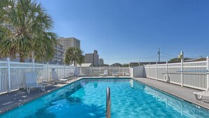 A swimming pool with a white fence, lounge chairs, and palm trees. - Beachfront Suite with Free WiFi, Elevator, Shared Pool, and Central AC (Orange Beach)