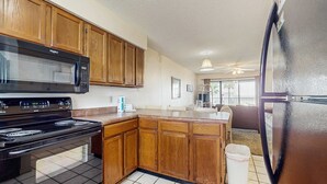 A kitchen with wooden cabinets, a black stove, a microwave, and a refrigerator. - Beachfront Suite with Free WiFi, Elevator, Shared Pool, and Central AC (Orange Beach)