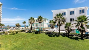 A hotel with a white building, a green and white structure, and palm trees in the foreground. - Beachfront Suite with Free WiFi, Elevator, Shared Pool, and Central AC (Orange Beach)