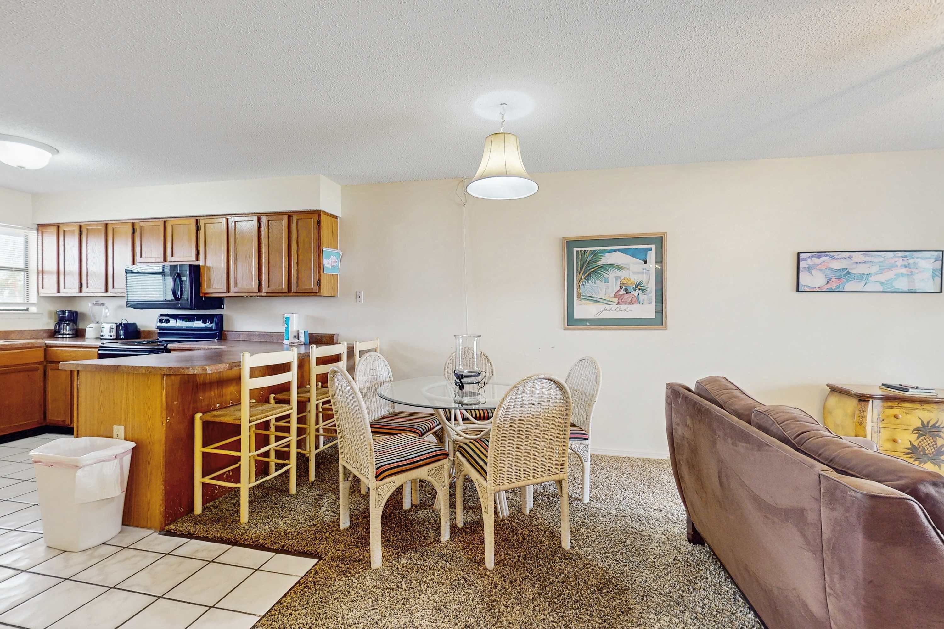 A kitchen with wooden cabinets, a microwave, and a dining area with wicker chairs.