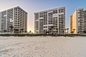 Ein Hotel direkt am Strand mit mehreren Etagen, Balkonen und einem sandigen Strand im Vordergrund.
