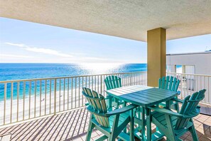 A balcony with a table and chairs, overlooking a beach and ocean. - Gulf-front condo with pool, hot tub, sauna, gym, AC, cable, & washer/dryer (Orange Beach)