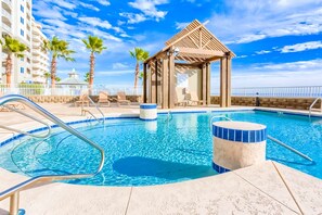 A swimming pool with lounge chairs, a wooden gazebo, and palm trees. - Gulf-front condo with pool, hot tub, sauna, gym, AC, cable, & washer/dryer (Orange Beach)