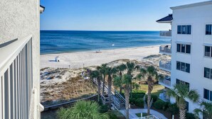 Un hôtel situé en bord de mer, doté de balcons offrant une vue sur la plage, les palmiers et une vue dégagée sur l’océan.