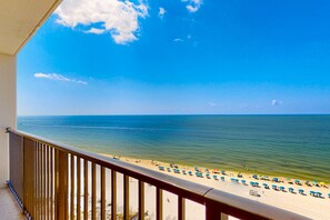 Ein Balkon mit Blick auf einen Strand, einem Geländer und einem wolkenlosen Himmel.