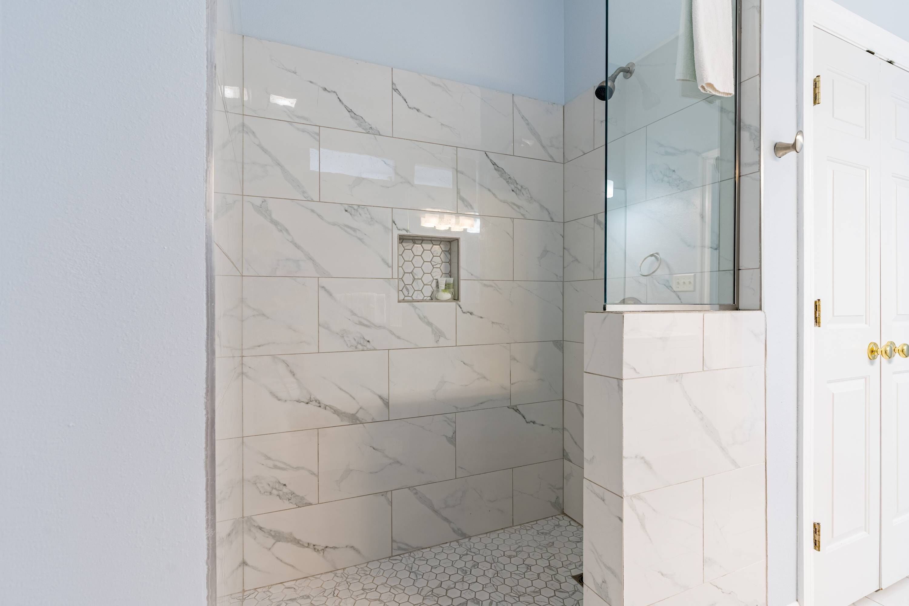 Une salle de bain avec des carreaux de marbre blanc, un motif hexagonal sur le sol et une cabine de douche en verre.