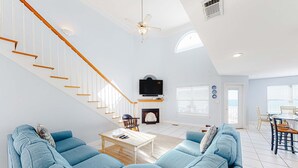 Un salón amplio con un sofá azul, una mesa de centro de madera, una chimenea, un televisor y una escalera.